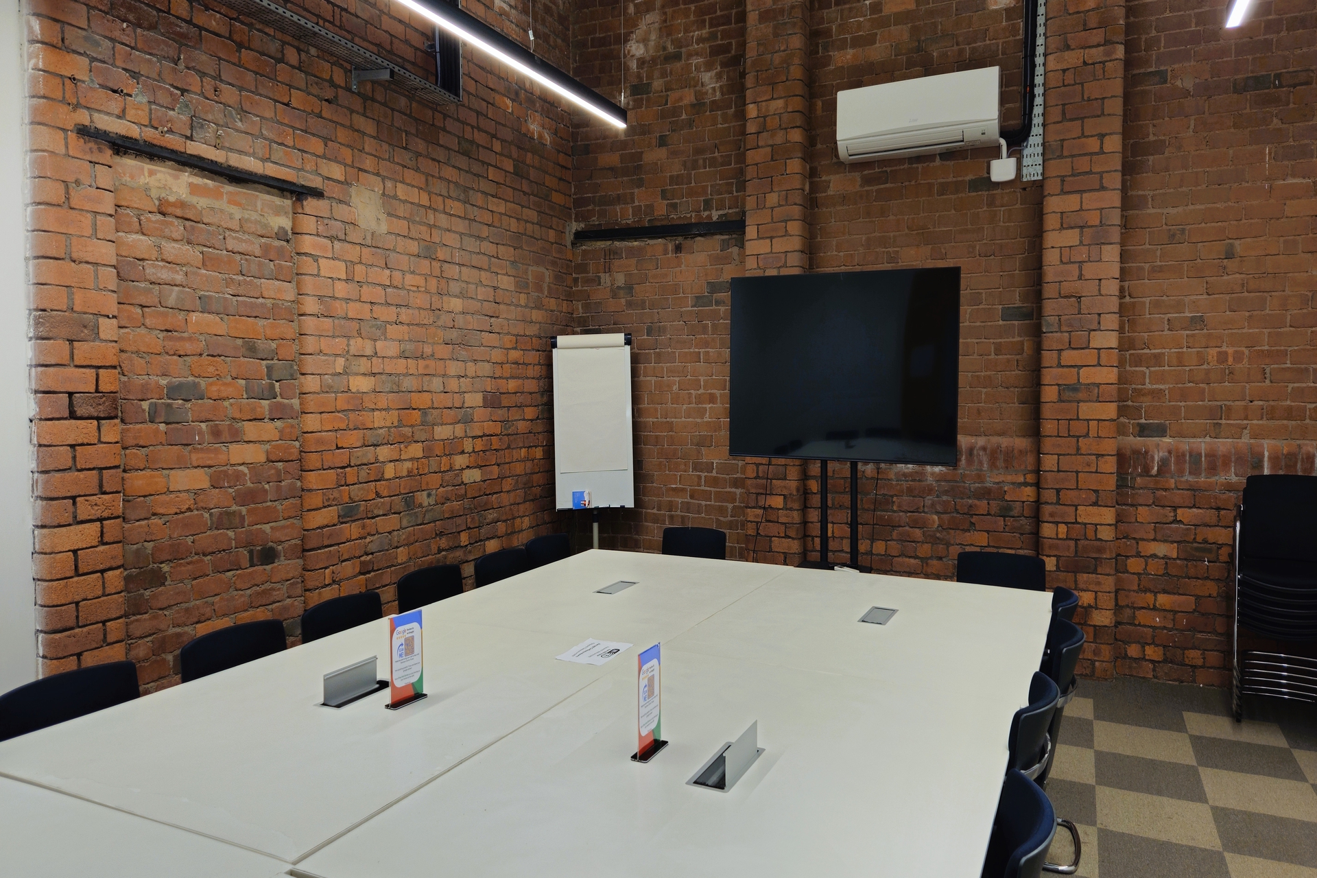 professional meeting room at Ram Mill Business Centre in Oldham, featuring exposed brick walls, a large display screen, flipchart, and modular table setup. Perfect for team discussions, strategy sessions, and workshops.