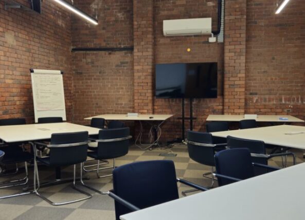 professional meeting room at Ram Mill Business Centre in Oldham, featuring exposed brick walls, a large display screen, flipchart, and modular table setup. Perfect for team discussions, strategy sessions, and workshops.