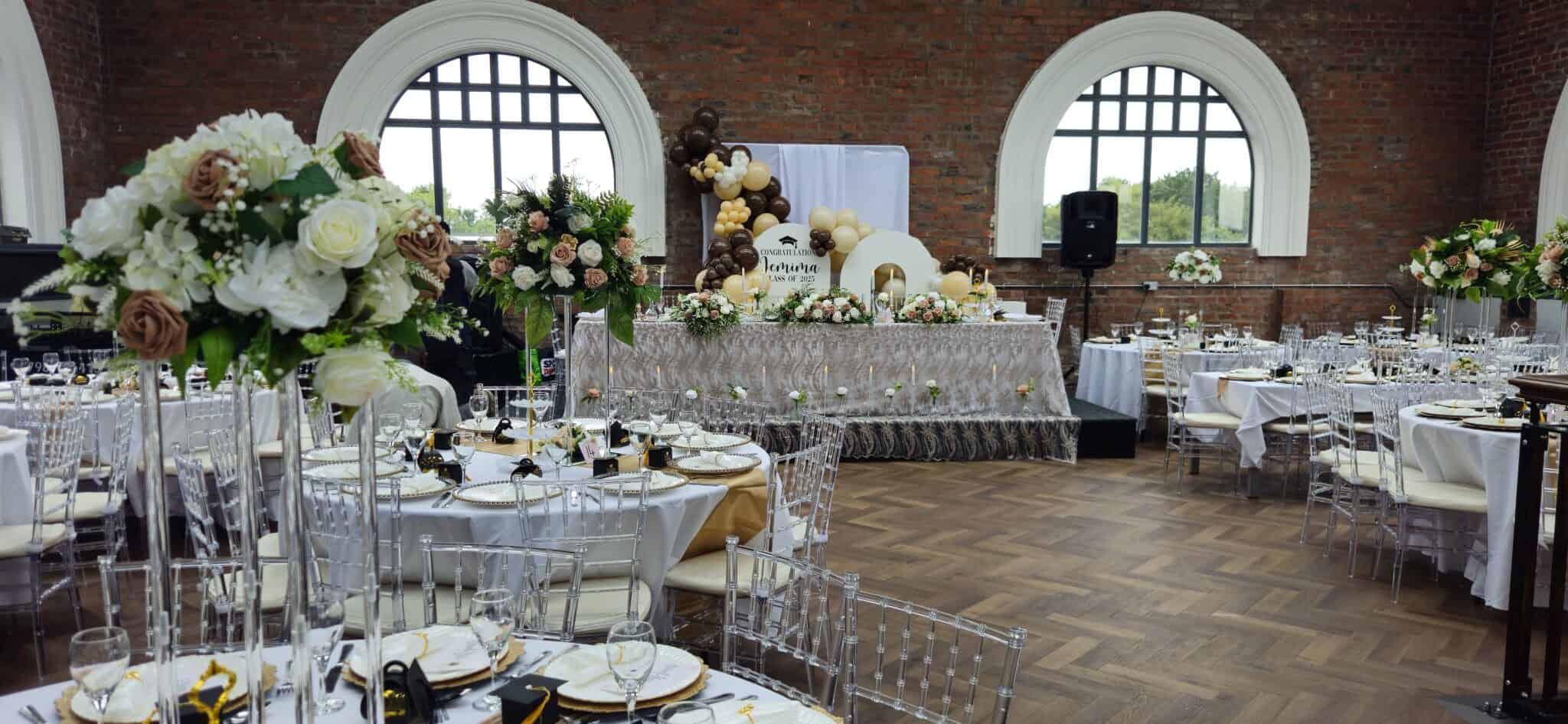 Dining tables with tall floral centrepieces under arched windows
