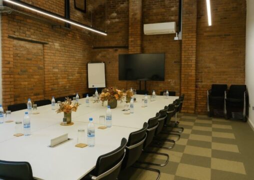 Meeting Room 2 professional meeting room at Ram Mill Business Centre in Oldham, featuring exposed brick walls, a large display screen, flipchart, and modular table setup. Perfect for team discussions, strategy sessions, and workshops.