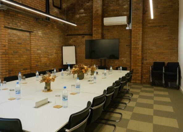 professional meeting room at Ram Mill Business Centre in Oldham, featuring exposed brick walls, a large display screen, flipchart, and modular table setup. Perfect for team discussions, strategy sessions, and workshops.